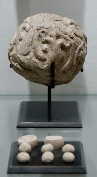 Globular envelope with a cluster of accounting tokens. Clay, Uruk period. From the Tell of the Acropolis in Susa.  An inscribed token used in commercial and legal documentation as a form of authentication and for tamper-proofing whatever is attached to it (or&nbsp;contained in it). The picture shows a ball of clay with figures marked on it, together with round clay counting tokens